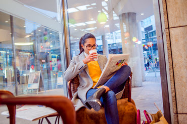 jeune femme assise sur un fauteuil buvant son café en lisant les dernières nouvelles