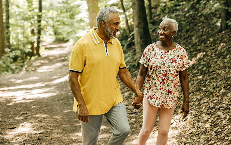 Deux retraités un homme et une femme noirs prenant une marche sur un sentier en pleine nature.