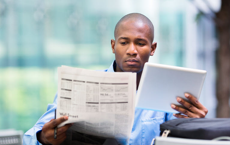 homme afro-américain comparant observant les cours de la bourse sur sa tablette et dans le journal.
